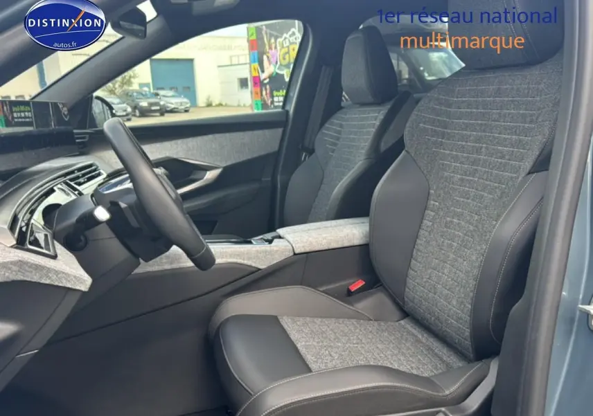 Vue intérieure côté conducteur du Peugeot 3008 bleu 2025, sièges tissu et cuir gris avec accoudoir central.