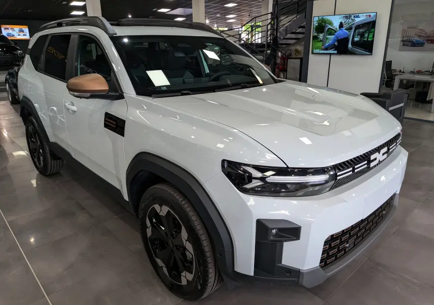 SUV Dacia Bigster blanc glacier en 3/4 avant droit, avec rétroviseurs bronze et jantes noires distinctives.