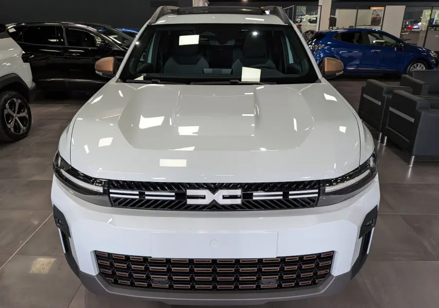 Vue frontale d'un Dacia Bigster blanc glacier avec calandre noire et détails cuivrés en showroom.