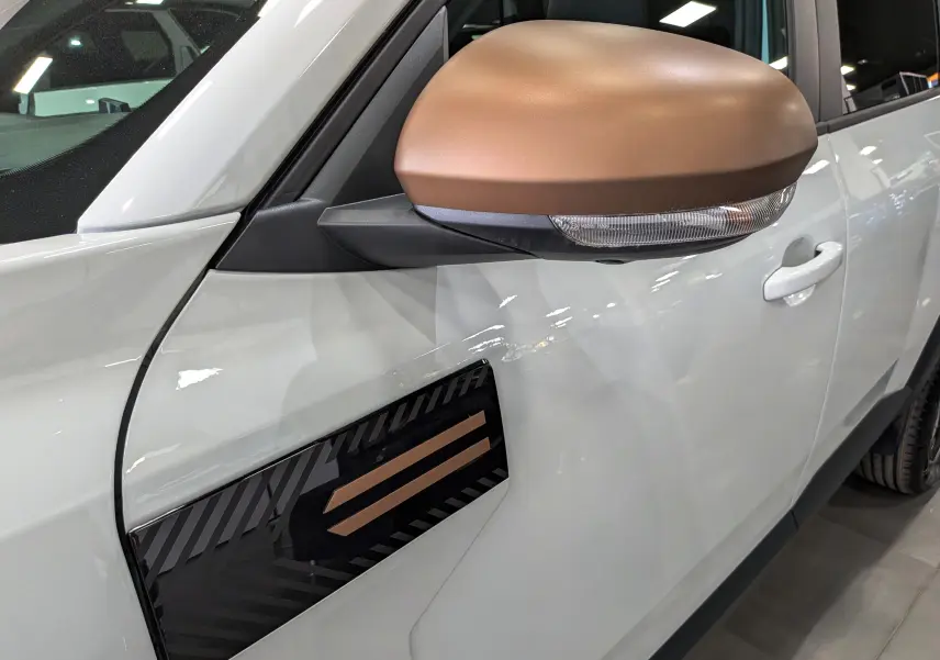 Détail du côté gauche du DACIA Bigster blanc Glacier, avec rétroviseur marron et insert décoratif noir et bronze.
