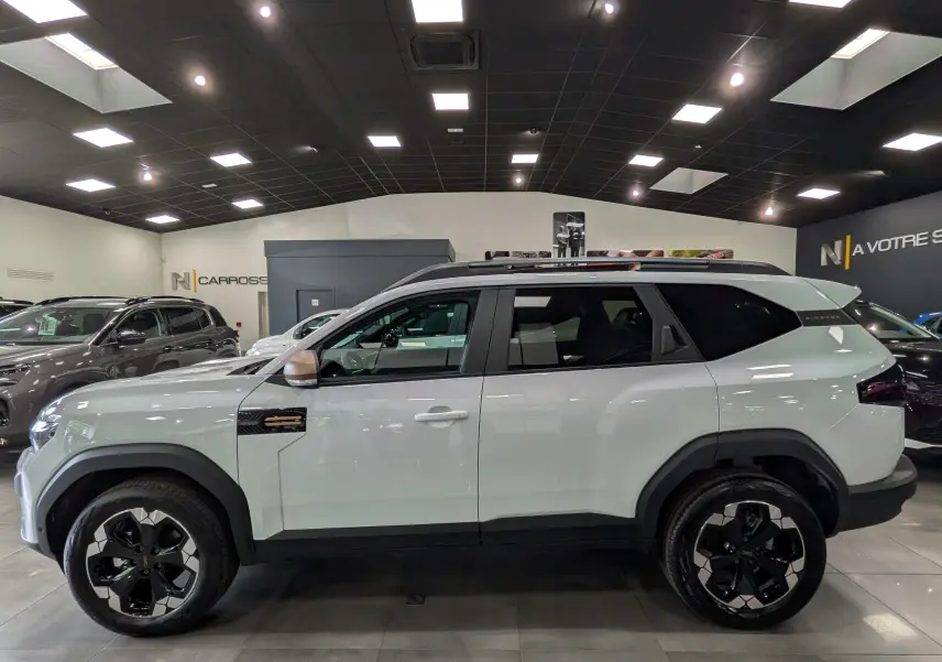 Profil droit du Dacia Bigster blanc Glacier 2026 avec jantes noires et toit ouvrant en showroom.