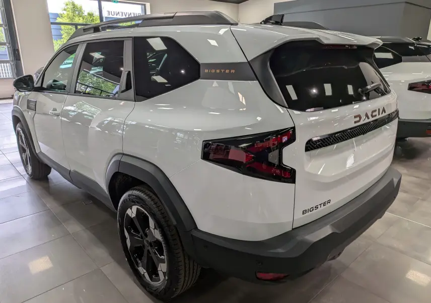 Vue 3/4 arrière droite du Dacia Bigster blanc Glacier, avec logo et feux arrière au design moderne en showroom.