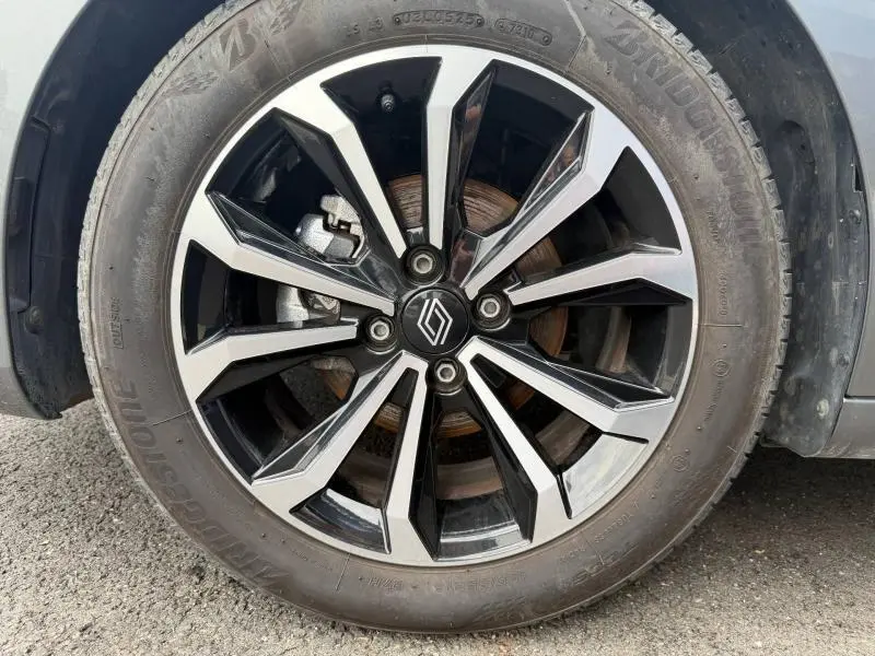 Gros plan sur la jante alu noire et argentée avec logo Renault, entourée du pneu Bridgestone sur Clio gris Schiste.