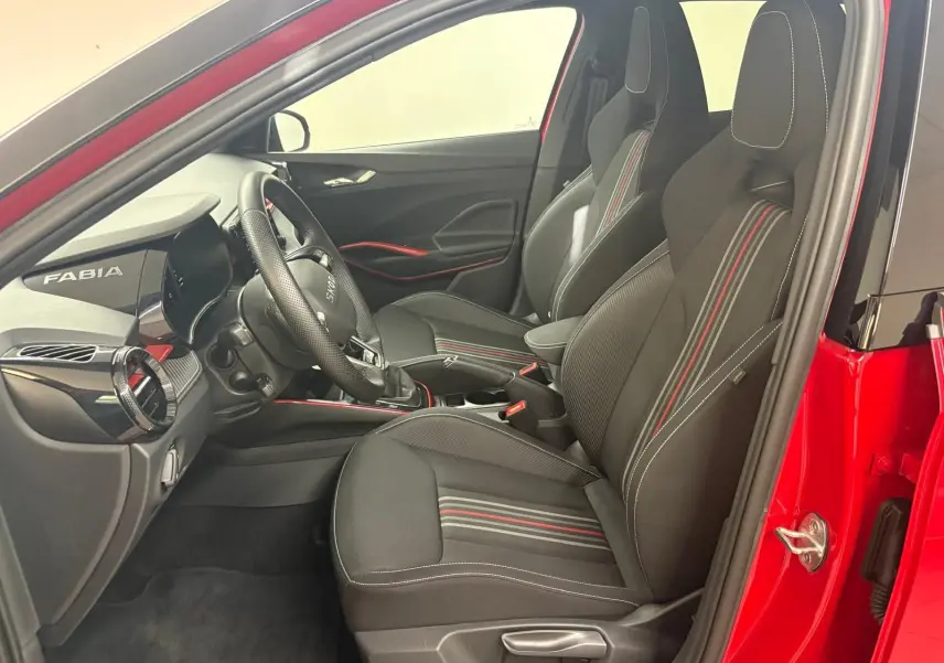 Vue intérieure côté conducteur de la Skoda Fabia rouge velvet avec sièges sport noirs à surpiqûres rouges et toit noir.