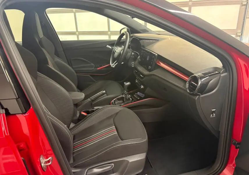 Vue intérieure côté conducteur d'une Skoda Fabia rouge velvet avec détails noirs et touches rouges sur tableau de bord et sièges.