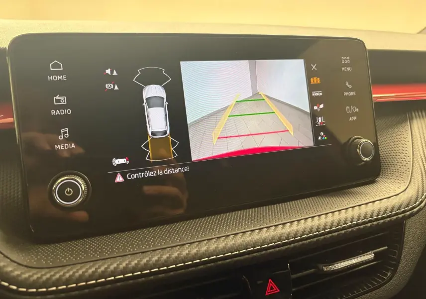 Écran central de la Skoda Fabia 2025 montrant la caméra de recul et l'alerte de distance, avec finition intérieure noire et rouge.