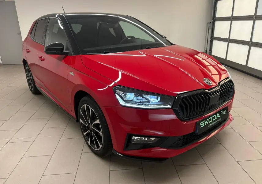 Vue 3/4 avant gauche d'une Skoda Fabia Monte Carlo rouge Velvet avec toit noir et phares allumés en intérieur.