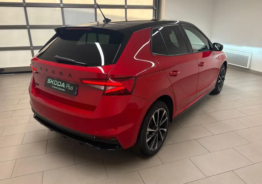 Vue 3/4 arrière droite d'une Skoda Fabia 1.0 TSI Monte Carlo rouge Velvet avec toit noir dans un showroom.