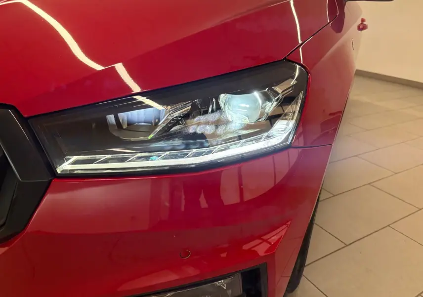 Gros plan sur le phare avant droit d’une Skoda Fabia 2025 rouge Velvet avec toit noir, éclairage LED allumé.