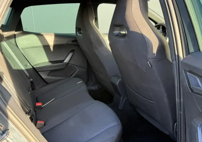 Vue intérieure côté arrière droit de la SEAT IBIZA TSI 115 FR 2025 avec sièges tissu noirs et garnitures sombres.