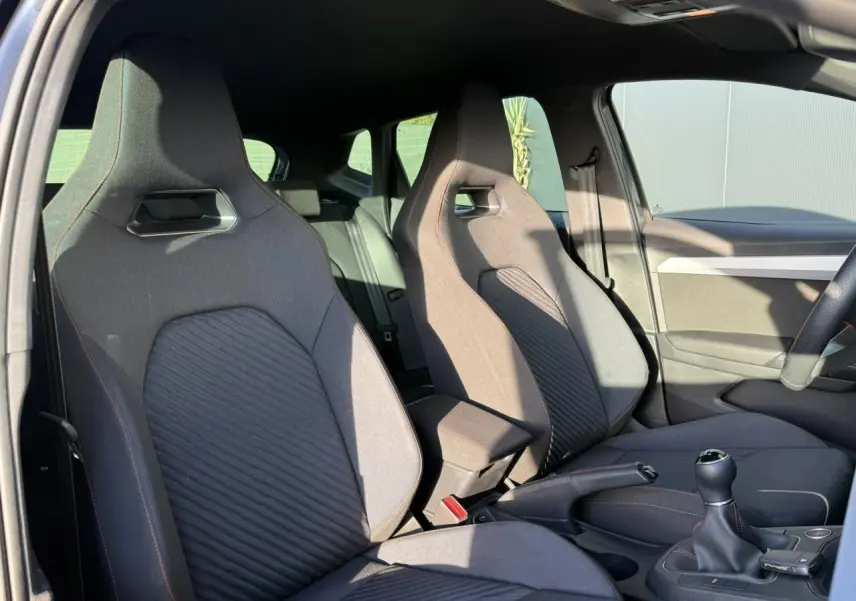 Intérieur de la SEAT IBIZA TSI 115 FR 2025, vue côté conducteur, sièges sport gris avec surpiqûres rouges.