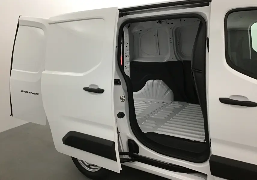 Vue latérale droite d’un Peugeot Partner blanc 2025 avec porte coulissante ouverte montrant l’espace de chargement vide.