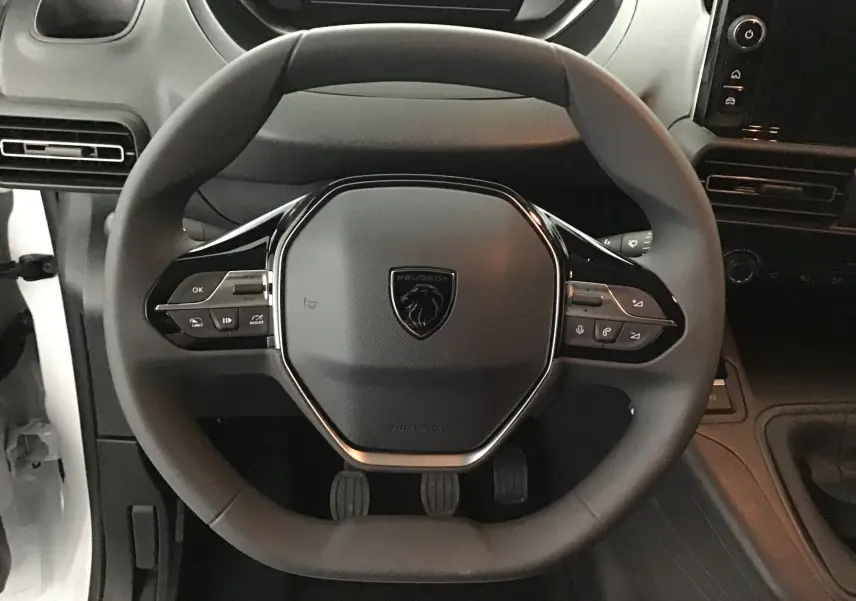 Vue rapprochée du volant noir du Peugeot Partner 2025 avec commandes intégrées et tableau de bord sombre.