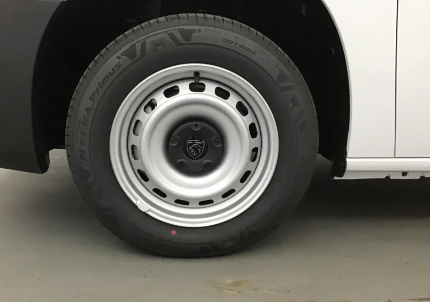 Gros plan sur la roue avant gauche du Peugeot Partner blanc 2025, mettant en valeur la jante acier et le logo central.