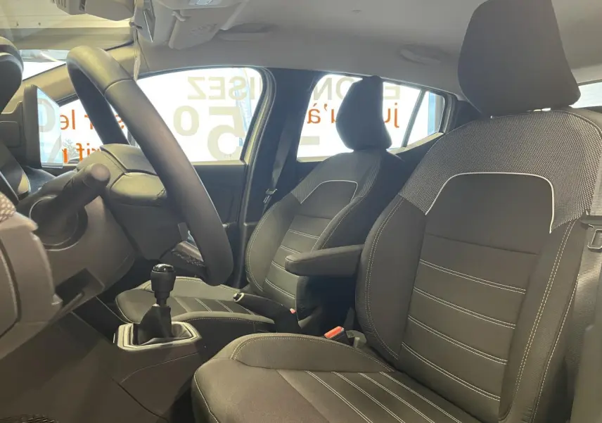 Vue intérieure côté conducteur de la Dacia Sandero Stepway 2025, sièges noirs avec coutures blanches et accoudoir central.