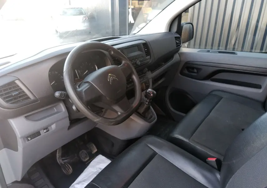 Vue intérieure côté conducteur du Citroën Jumpy blanc 2021, montrant le volant, tableau de bord et sièges noirs.