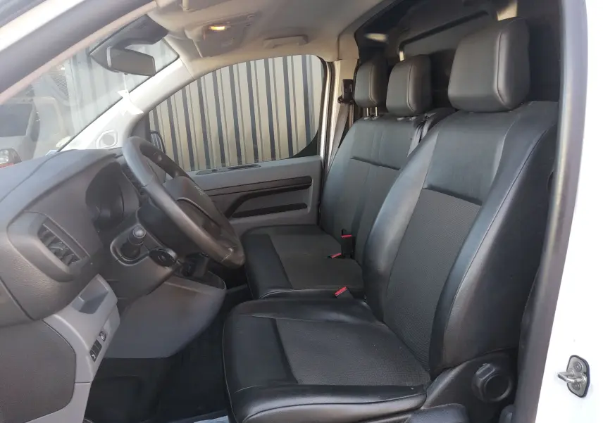 Vue intérieure côté conducteur du Citroën Jumpy blanc 2021, montrant les sièges en cuir noir et le volant multifonction.
