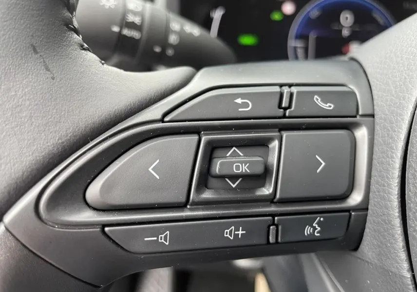 Gros plan sur les commandes multifonctions noires du volant côté gauche d'une Toyota Yaris Cross gris clair 2026.