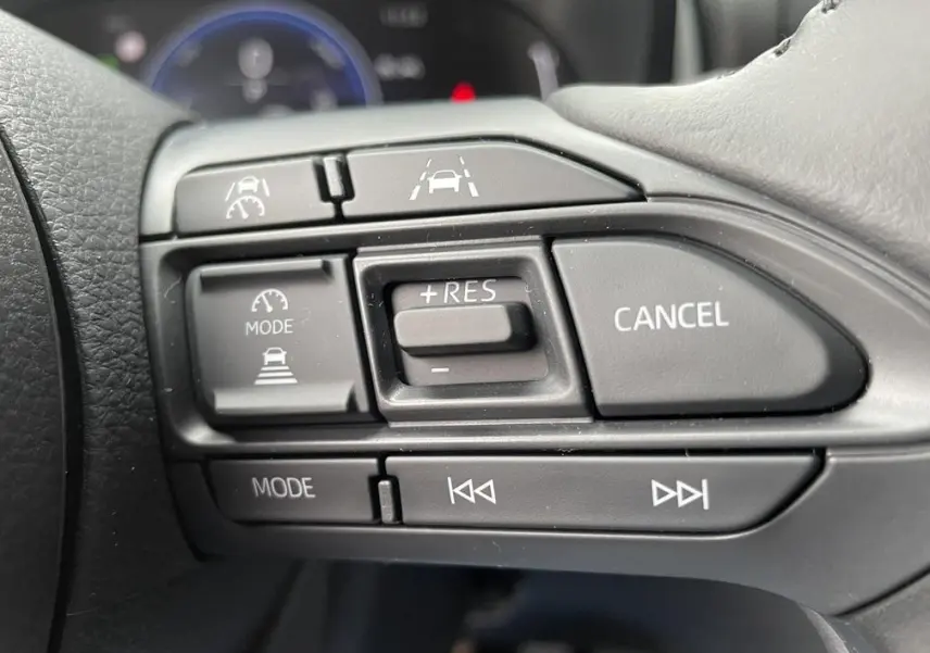 Gros plan sur les commandes du régulateur de vitesse au volant d’une Toyota Yaris Cross gris clair.