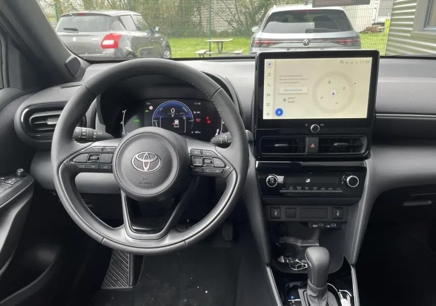 Vue intérieure avant de la Toyota Yaris Cross 2026, tableau de bord noir avec écran tactile central et volant multifonctions.