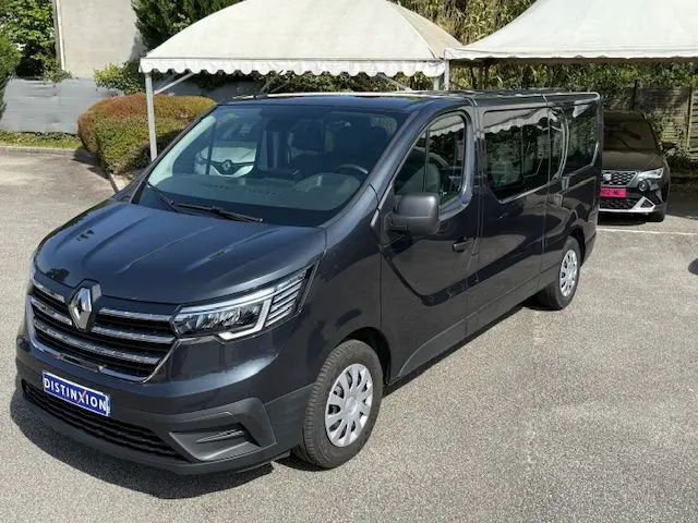 Vue 3/4 avant droit d'un Renault Trafic Combi gris comète, avec calandre chromée et phares LED distinctifs.
