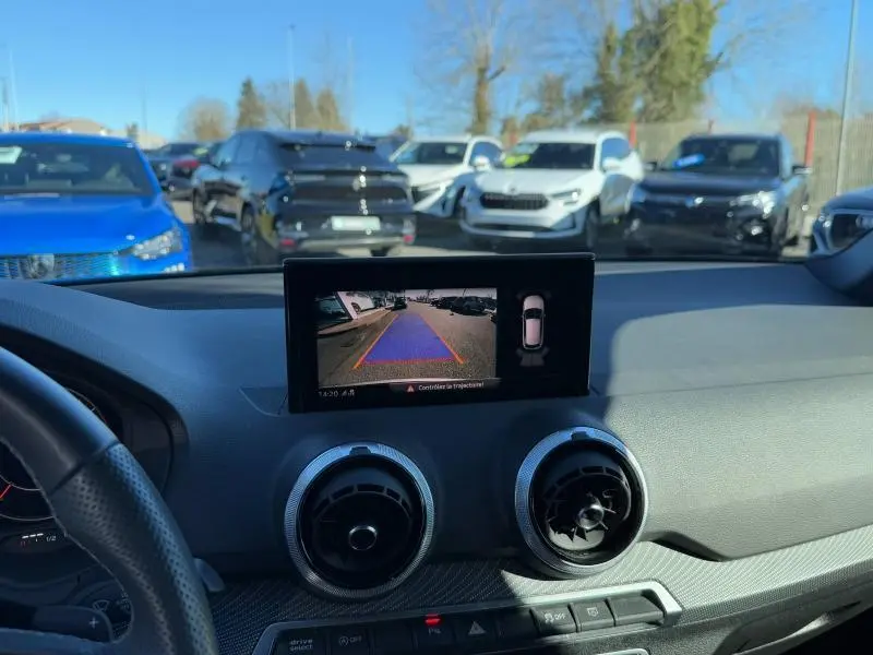 Vue intérieure du tableau de bord d'un Audi Q2 noir avec écran central affichant la caméra de recul en marche.