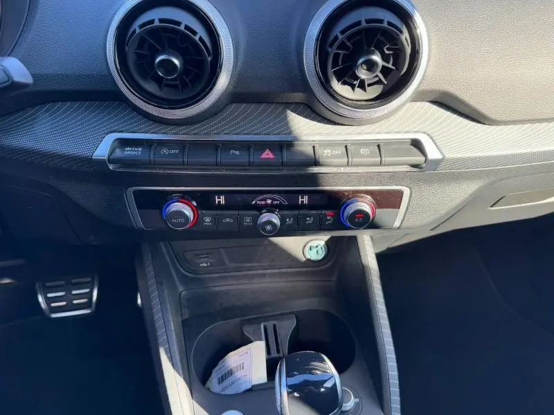 Vue rapprochée de la console centrale de l'Audi Q2 30 TDI 2024, avec commandes climatisation et aérateurs ronds noirs.