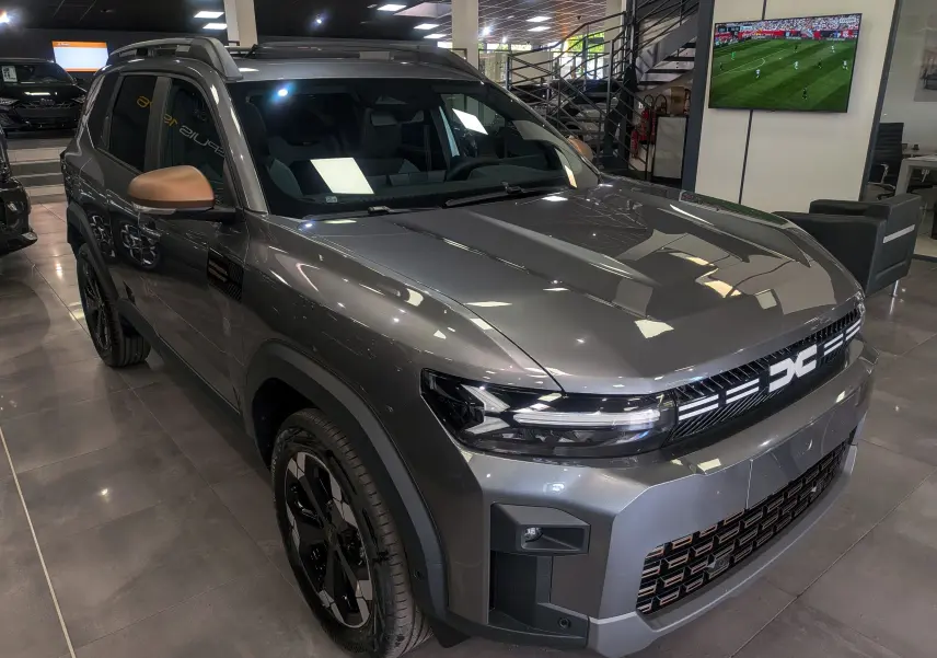 Vue 3/4 avant droit du Dacia Bigster gris schiste avec détails noirs et rétroviseurs couleur cuivre en showroom.