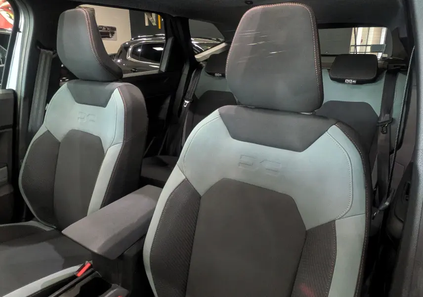 Vue intérieure rapprochée des sièges avant en tissu gris clair et foncé du Dacia Bigster Mild Hybrid 2026, avec surpiqûres rouges.