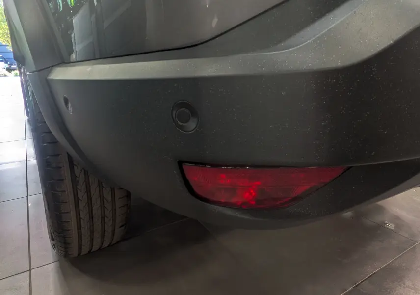 Gros plan sur le pare-chocs arrière gris schiste du Dacia Bigster, avec feu rouge et capteurs de recul visibles.