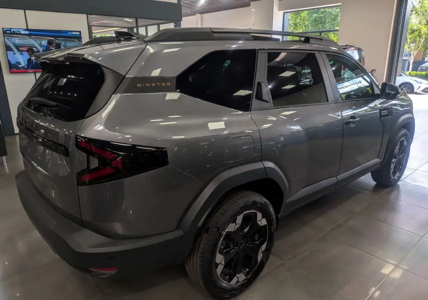 Vue 3/4 arrière droite du Dacia Bigster gris schiste avec jantes noires et toit avec barres de toit en concession.