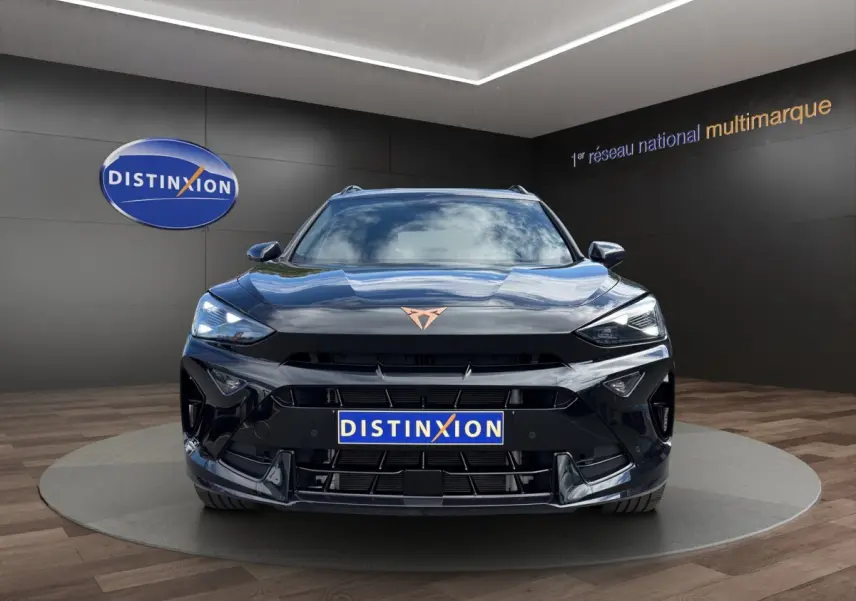 Vue frontale d'un CUPRA Formentor noir brillant avec logo cuivré, dans un showroom au sol bois et mur sombre.