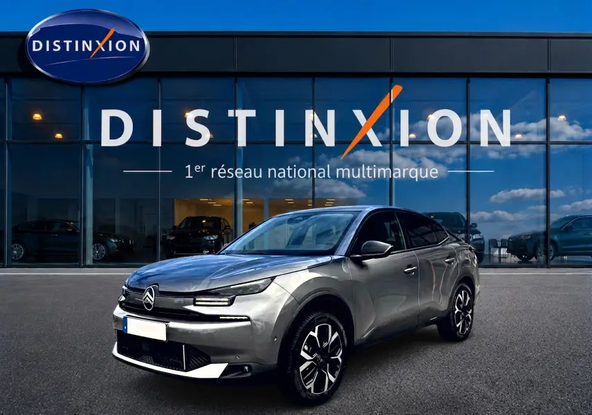 Citroën C4 X gris mercure en 3/4 avant droit, avec jantes alu et calandre distinctive, devant un showroom Distinxion.
