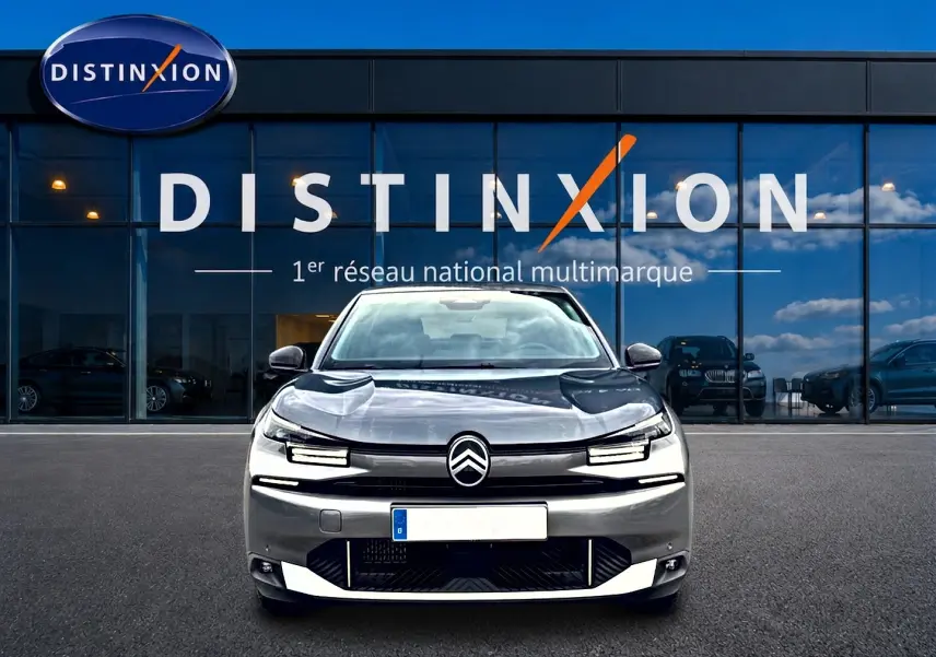 Vue frontale d'une Citroën C4 X gris mercure 2025 avec phares LED et calandre distinctive, devant une vitrine Distinxion.
