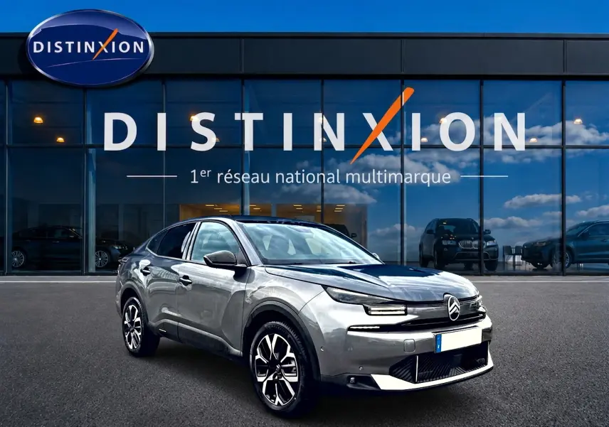 Citroën C4 X gris mercure en 3/4 avant droit, avec jantes alu et calandre distinctive devant un showroom Distinxion.