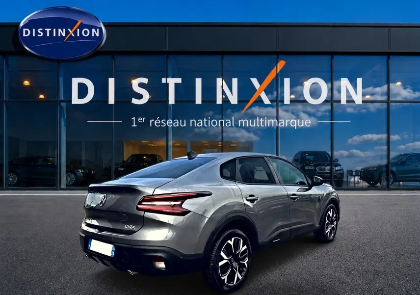 Vue 3/4 arrière droite d'une Citroën C4 X gris mercure avec feux LED et jantes alliage devant un showroom Distinxion.