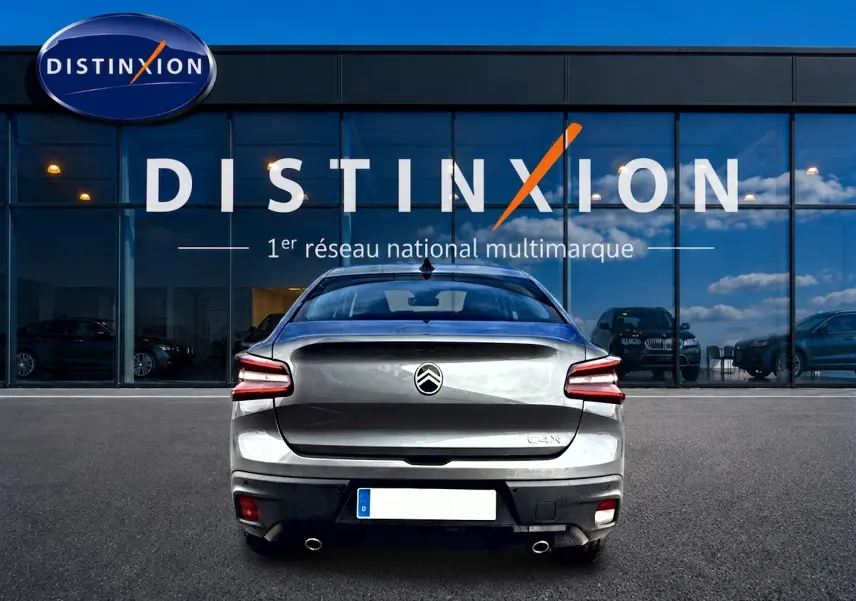 Vue arrière d'une Citroën C4 X gris mercure stationnée devant une vitrine avec logo Distinxion.