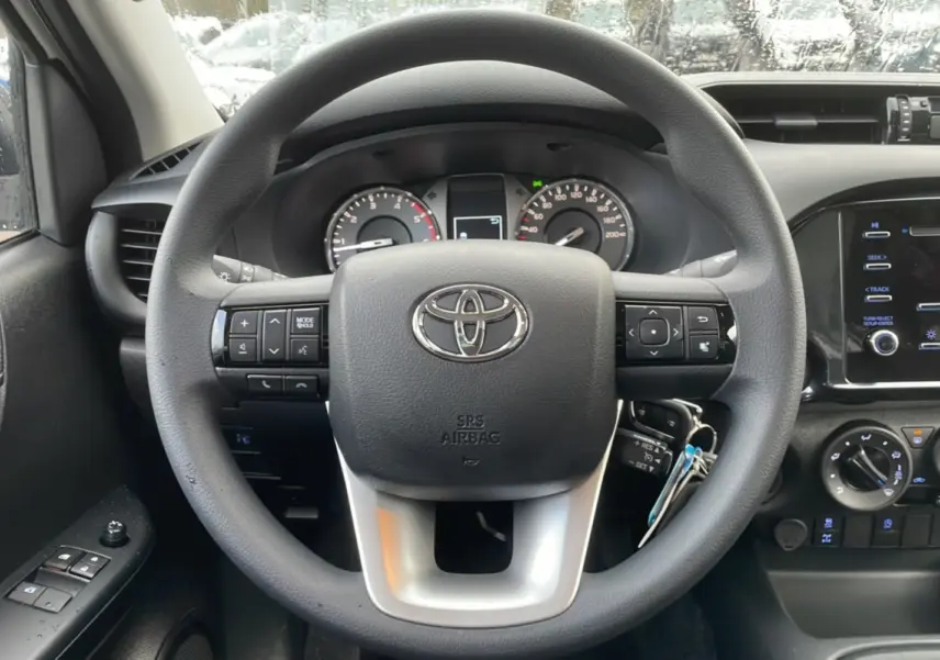 Vue intérieure centrée sur le volant du Toyota Hilux 4x4 2024 avec commandes intégrées et tableau de bord noir.
