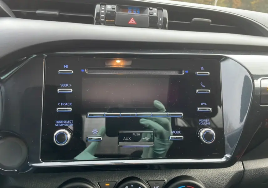 Vue rapprochée du tableau de bord noir du Toyota Hilux 2024, mettant en valeur l'écran tactile et les commandes audio.