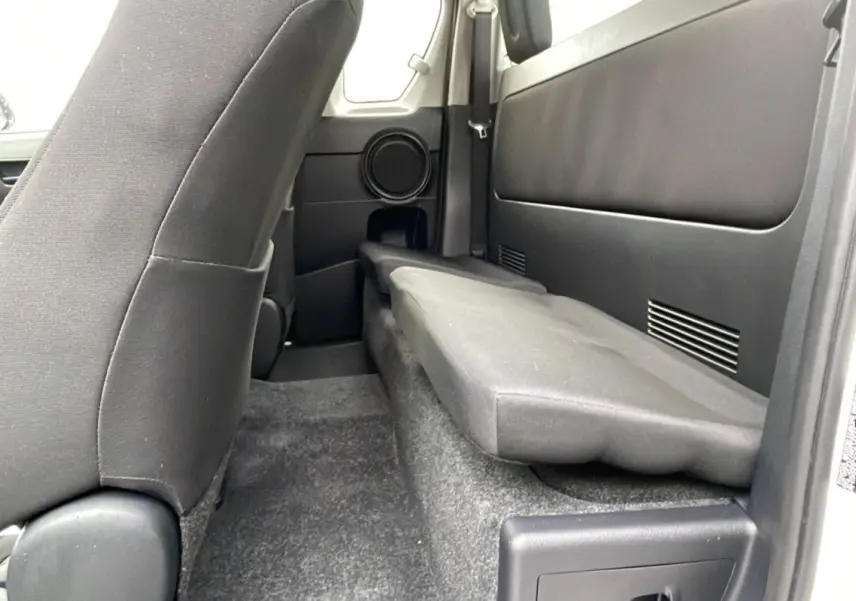 Vue intérieure arrière droite du Toyota Hilux 2024 blanc, montrant la banquette rabattue et les sièges noirs.