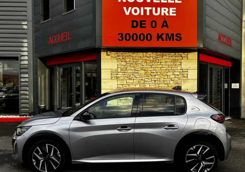 Peugeot 208 Hybrid 110 e-DCS6 GT gris clair vue de profil côté gauche devant un bâtiment avec panneau orange.