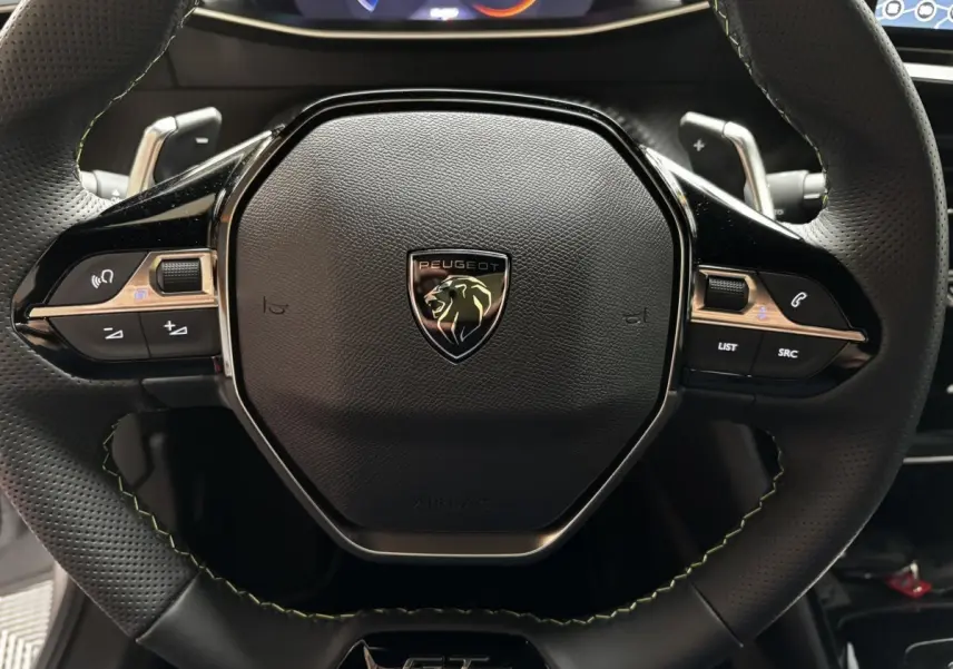 Gros plan sur le volant alu et cuir noir perforé du Peugeot 208 Hybrid 110 e-DCS6 GT avec logo lion central.
