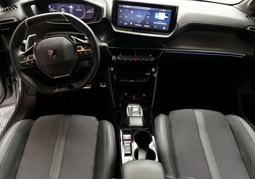 Intérieur de la Peugeot 208 Hybrid GT 2025, vue avant centrée sur le volant cuir alu et l’écran tactile central.