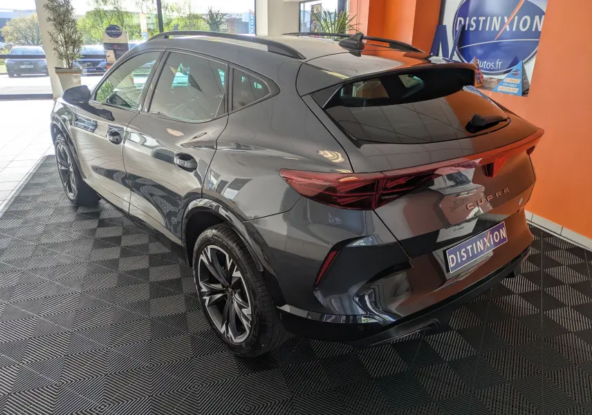 Vue 3/4 arrière droite du CUPRA Formentor gris magnétique avec jantes alliage 18'' bicolores et hayon électrique en intérieur showroom.