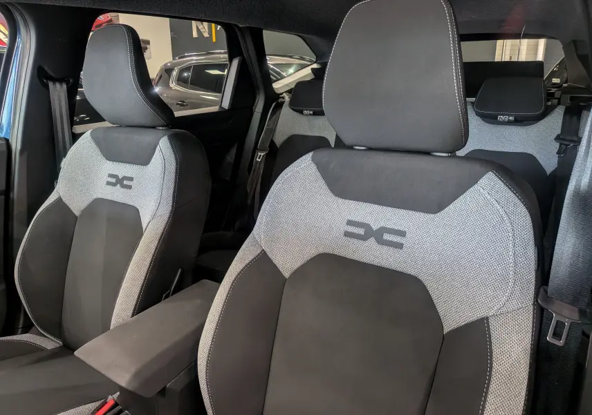 Gros plan sur les sièges avant tissu gris et noir du Dacia Bigster 2026, mettant en valeur le logo brodé sur les appuie-têtes.