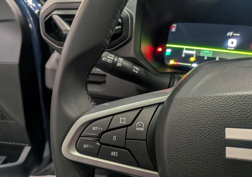 Gros plan sur le volant noir du Dacia Bigster 2026, avec commandes de régulateur et tableau de bord numérique en arrière-plan.