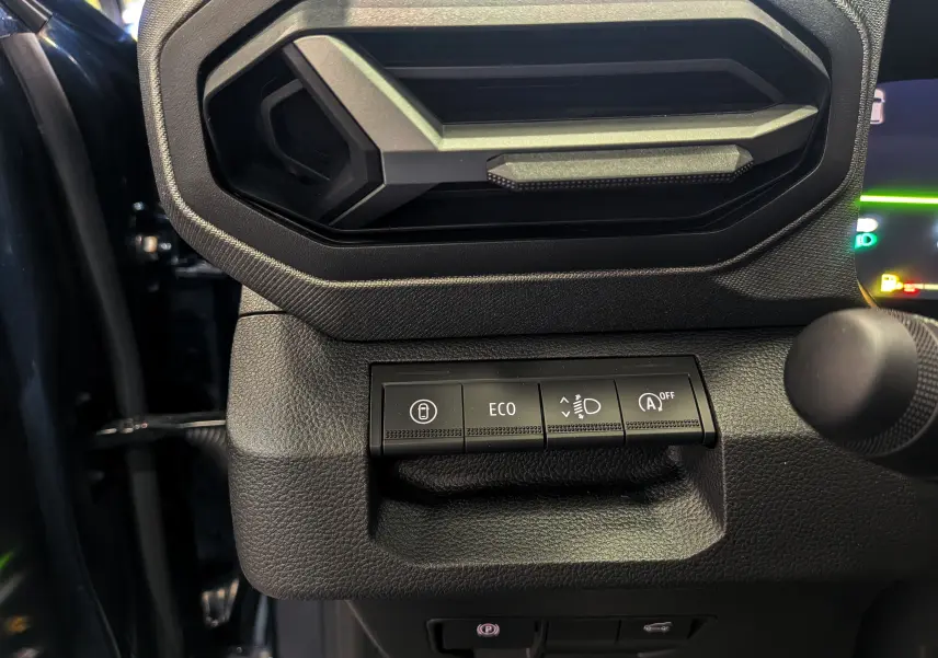 Gros plan sur les commandes sous la sortie d'air du tableau de bord noir du Dacia Bigster 2026, boutons ECO et verrouillage visibles.
