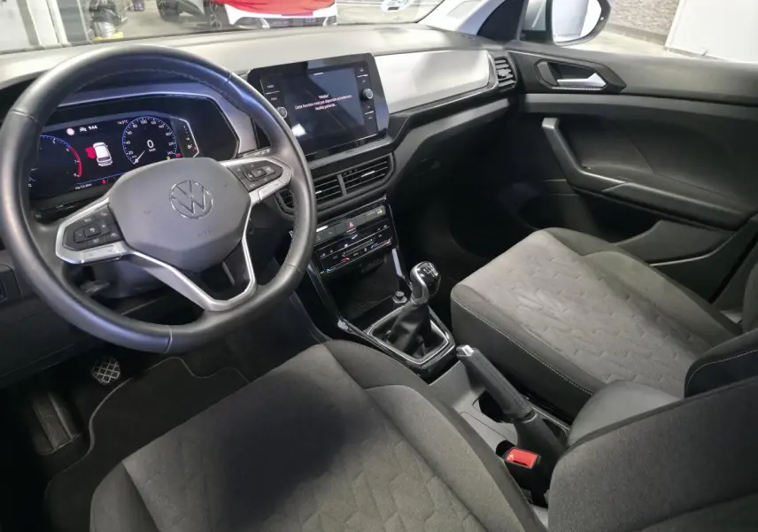 Vue intérieure côté conducteur du Volkswagen T-Cross 1.0 TSI 2025, avec volant cuir, tableau de bord digital et sellerie tissu gris.