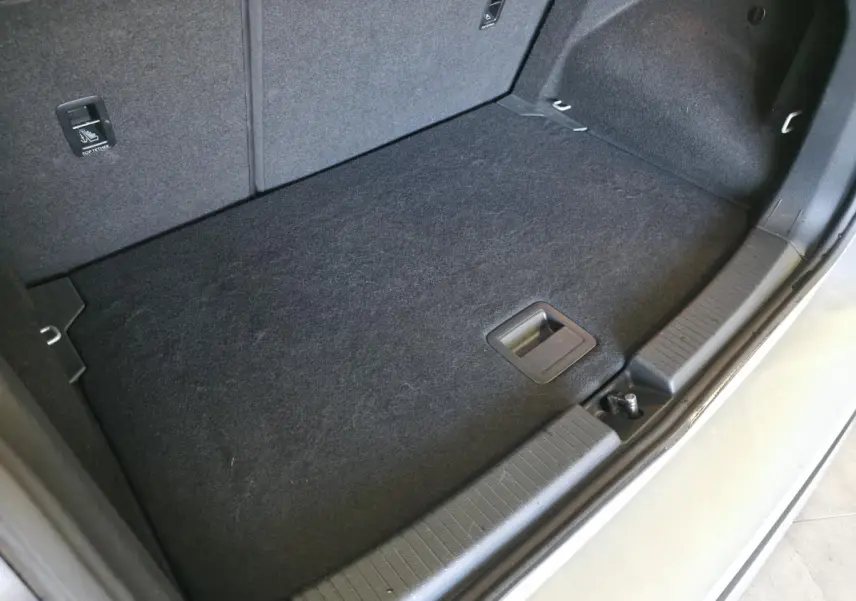 Vue rapprochée du coffre ouvert du Volkswagen T-Cross gris, montrant le tapis de sol et les finitions intérieures.