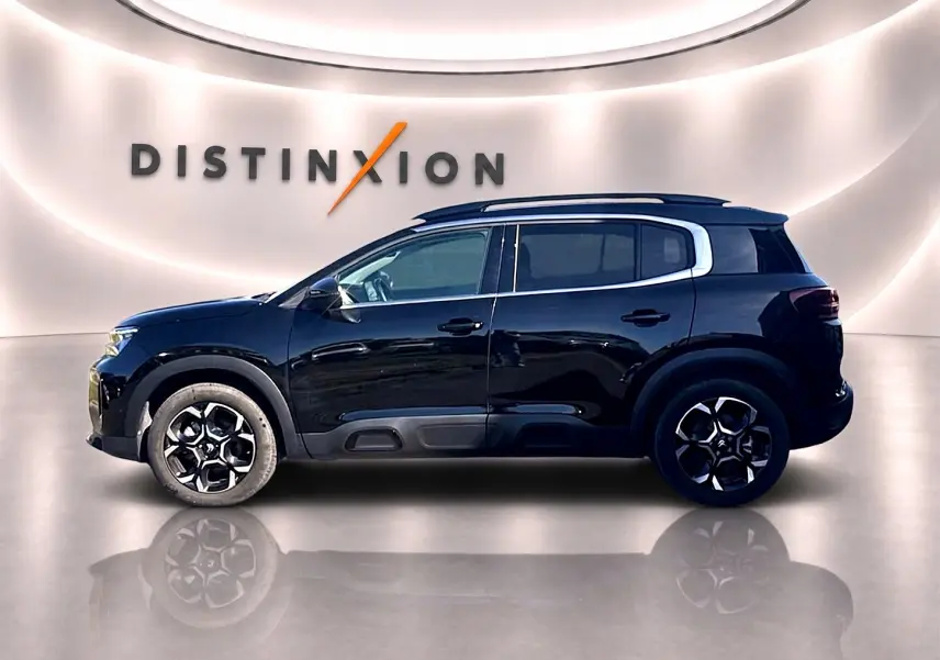 Profil droit d'un Citroën C5 Aircross noir 2025 avec barres de toit et jantes alliage distinctives, en studio lumineux.